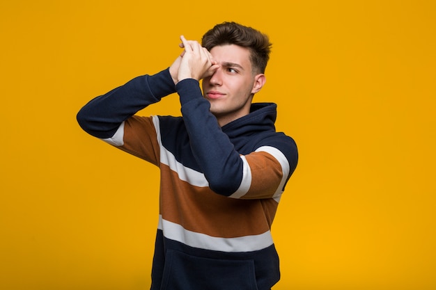 Photo young cool man wearing a hoodie looking far away keeping him hand on forehead.