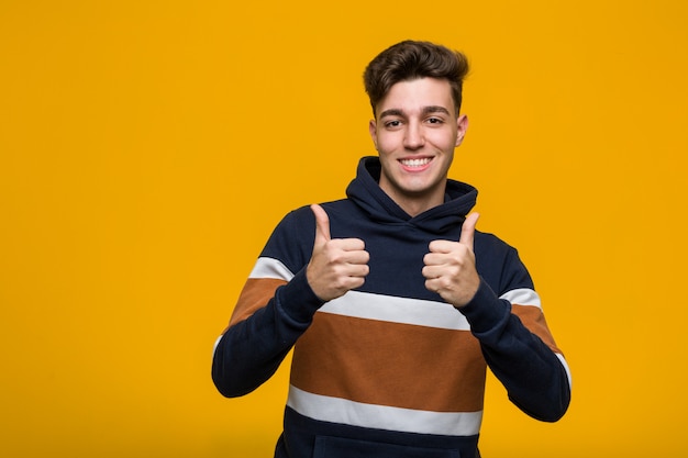 Young cool man wearing a hoodie raising both thumbs up, smiling and confident