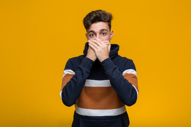 Young cool man wearing a hoodie shocked covering mouth with hands.