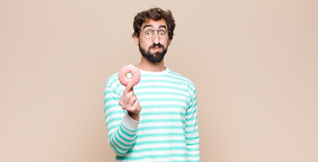 Young cool man with a sugar pink donut against flat wall