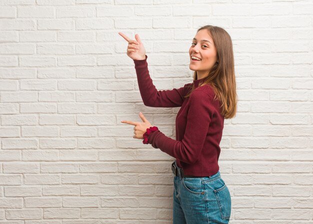 Giovane donna fredda su un muro di mattoni che punta verso il lato con un dito