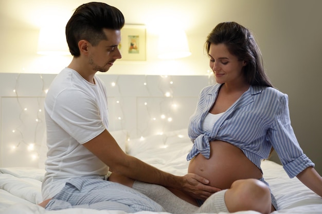 Young couple are waiting for a baby Husband and his pregnant wife relax on the bed at home