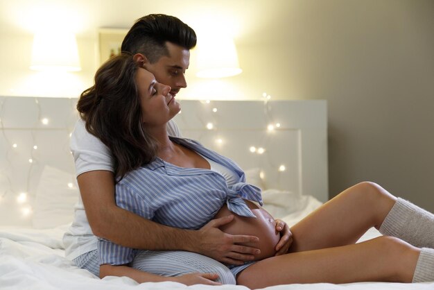 Young couple are waiting for a baby Husband and his pregnant wife relax on the bed at home