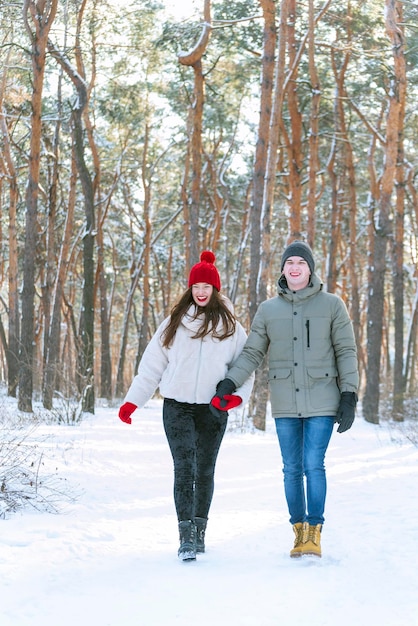 若いカップルが雪に覆われた森の晴れた日に歩いている森の冬の垂直フレーム