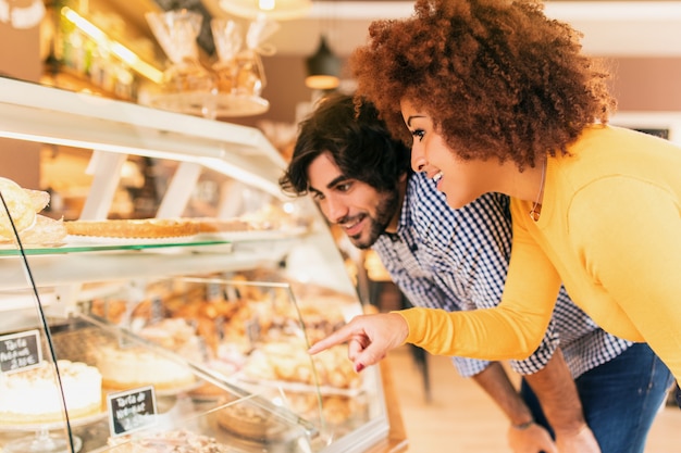 Young couple at bakery, looking at the showcase to eat something. They feel happy.