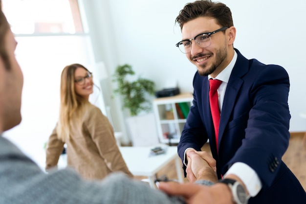 Young couple in bank office shaking hand to financial adviser.