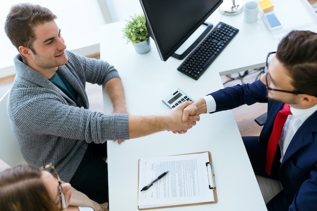 Young couple in bank office shaking hand to financial adviser.