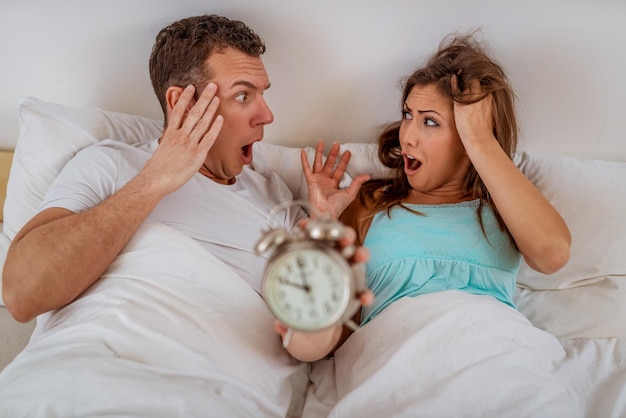 ベッドの中で若いカップルが目覚まし時計の鳴りに目覚めます。彼らは朝遅くです。