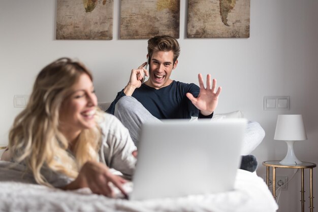 ベッドの上でコンピューターと電話を楽しんでいる若いカップル