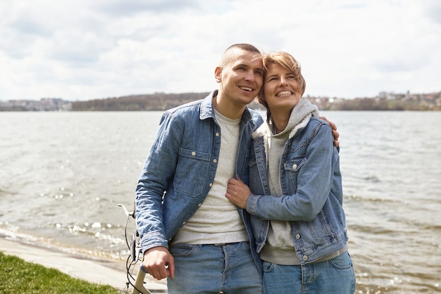 A young couple on a bicycle rides by the lake.