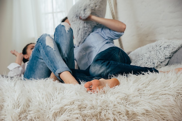 Photo a young couple in blue jeans having fun with pillows on hanged bed