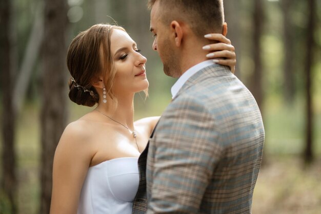 Young couple bride in a white short dress and groom in a gray suit in a pine forest