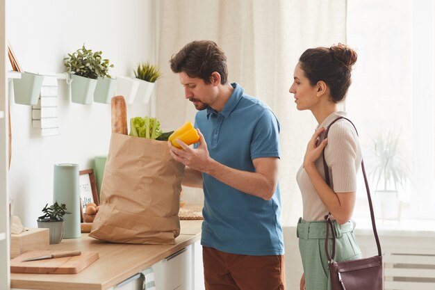 Young couple buying fresh vegetables in paper bag they bringing them to home in the kitchen