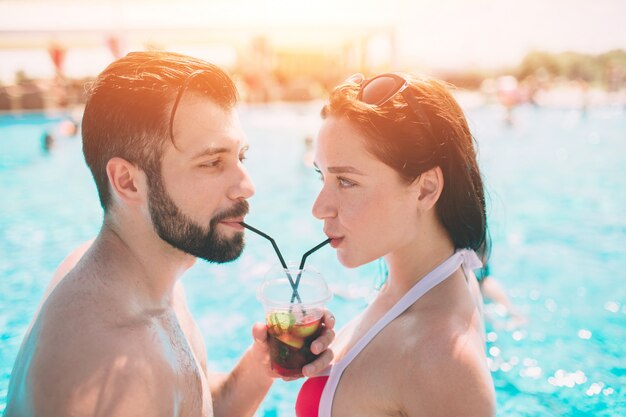 Coppia giovane a bordo piscina. uomo e donne che bevono i cocktail nell'acqua