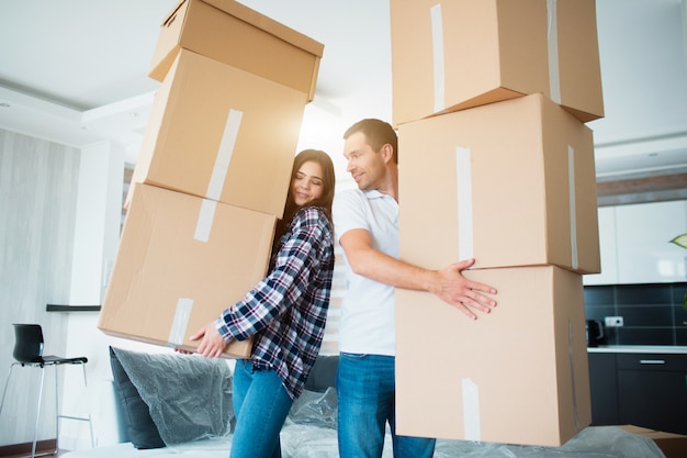 Young couple carrying many cardboard boxes one by one at new home. Moving house.