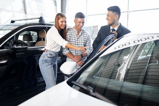 Young couple choosing a car at the dealership with manager helping