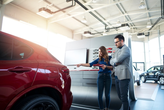 Young couple choosing favorite color for their brand new car at car dealership showroom.