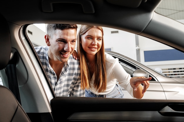 Young couple choosing their new car in a car shop together