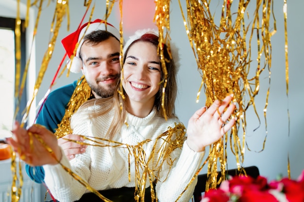 クリスマス帽子の若いカップルがクリスマスと新年の家を飾る