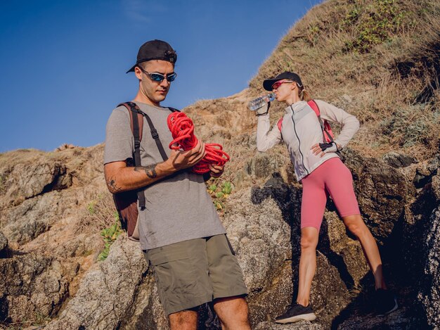 Young couple climbs with a rope to the top in the mountains near the ocean