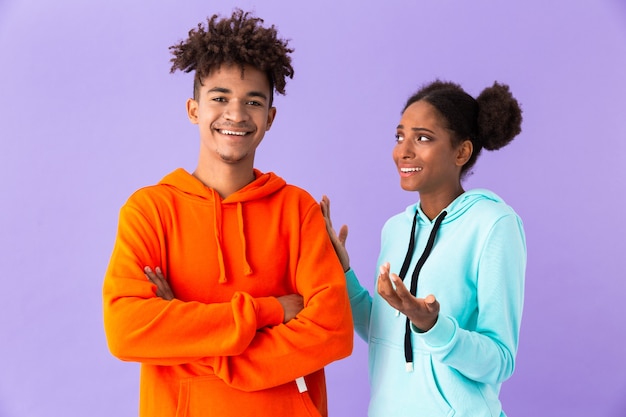 Photo young couple in colorful clothes talking together, isolated over violet wall