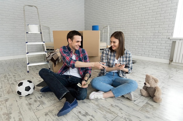 Молодая пара считает деньги, сидя на полу в новой квартире