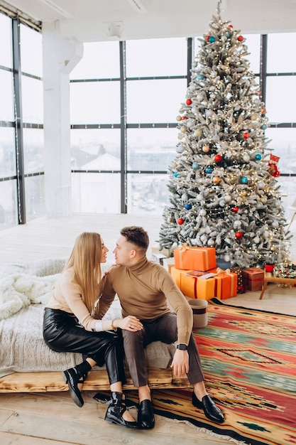 Young couple cuddle next to Christmas tree at home