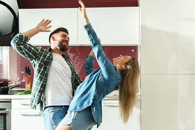 Young couple dancing on the kitchen while cooking during sunny morning