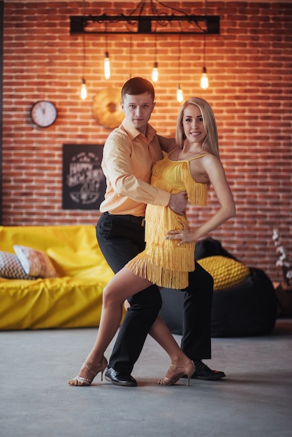 Young couple dancing latin music: Bachata, merengue, salsa. Two elegance pose on cafe with brick walls