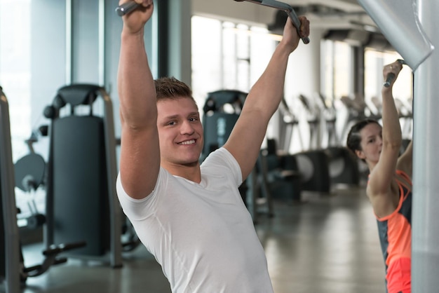 Young Couple Doing Exercise For Back On Machine In The Gym