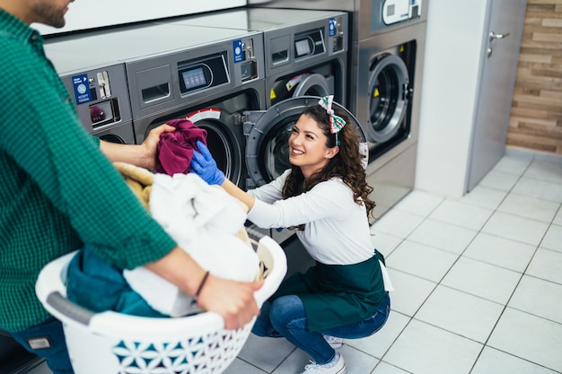 young couple doing laundry together at laundromat shop.