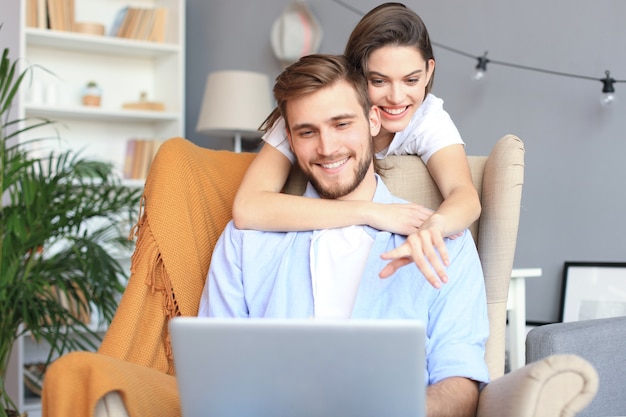 Young couple doing some online shopping at home, using a laptop on the sofa.