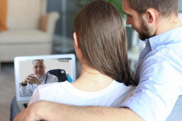 Young couple doing video conference with doctor on laptop