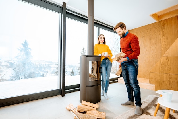 Young couple dressed in bright sweaters enjoying landscape view on the mountains standing together in the modern house during winter time