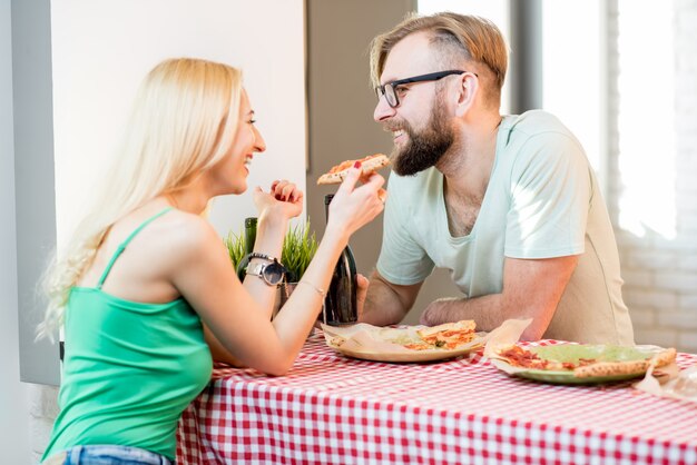 家でピザとビールと一緒に昼食をとるカジュアルな服を着た若いカップル