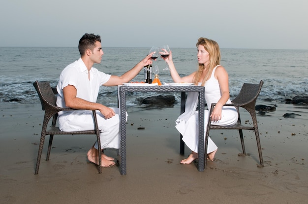 Young couple dressed in white celebrating a romantic dinner on the beach