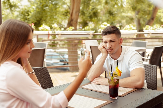 Молодая пара, пить кофе в кафе. Серьезный человек с тревогой смотрит в то время как его девушка с помощью смартфона