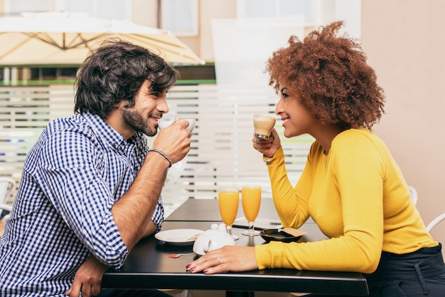Young couple drinking a coffee at cafe. They are smiling, looking at each other