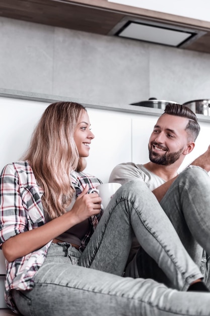 Young couple drinking coffee sitting on the kitchen floor