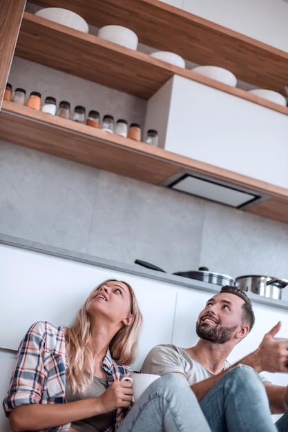 Young couple drinking coffee sitting on the kitchen floor