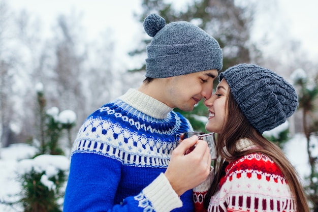 Young couple drinking tea in winter forest. happy people relaxing outdoors during holidays