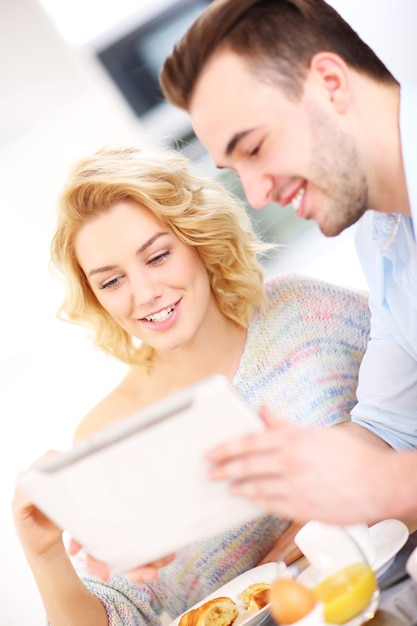 young couple eating breakfast in the kitchen and using tablet