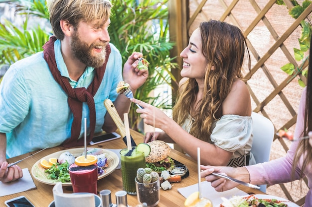 Le giovani coppie che mangiano il brunch e che bevono il frullato lanciano alla barra d'annata. persone felici pranzando sano e chiacchierando nel ristorante alla moda