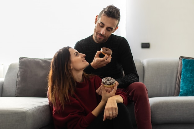 young couple eating a donut sitting on the carpet near a sofa