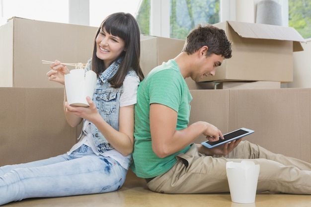 Young couple eating noodle and using digital tablet in their new house