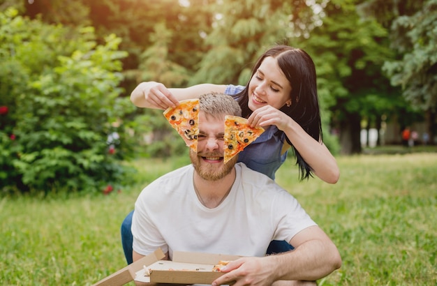 公園でピザを食べる若いカップル。彼らはお互いを扱い、笑います。