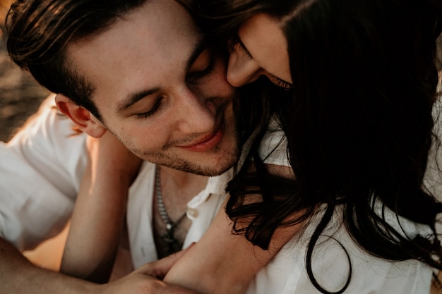 Young couple embracing and kissing on Sunset coast. Romantic love story. Brunette girl in a light dress.