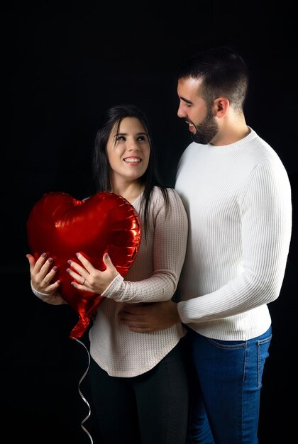 Giovani coppie che si abbracciano con cuore rosso su sfondo scuro