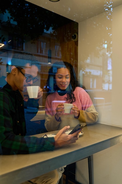 Young couple enjoying coffee and using smartphone in cafe