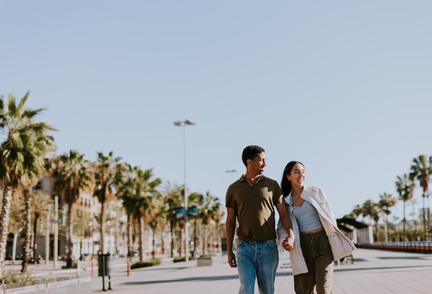 Foto giovane coppia che si godono una passeggiata soleggiata lungo la passeggiata palmate di barcellona